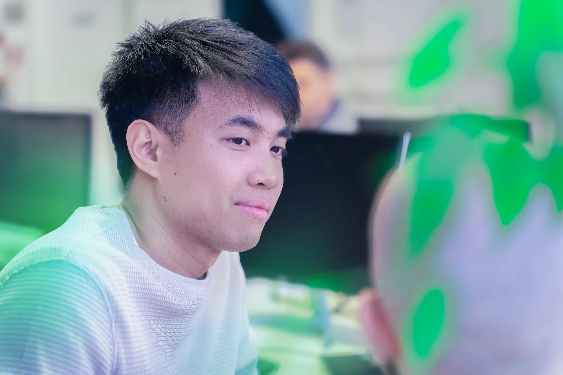 Collega di Winet in primo piano che ascolta con attenzione durante una conversazione in ufficio su progetti software per Thales, circondato da monitor e piante verdi.